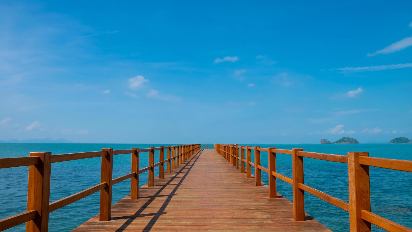 Outdoor, landscape shot of wooden walk way into the middle of the ocean. With clear blue sky and cloud with seascape island view. Tropical travel destination ideal for background with copy space. photo