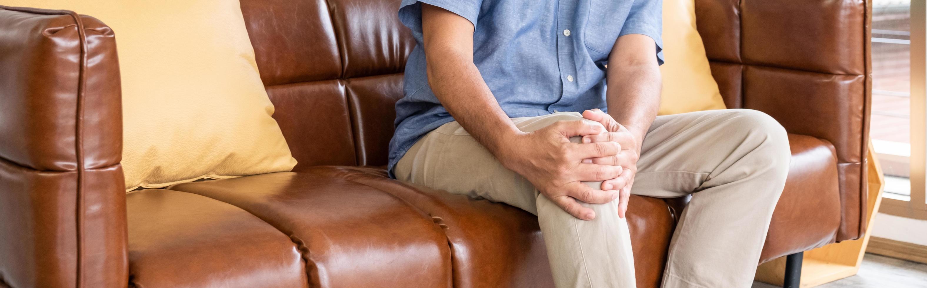 Selective focus at hand. Banner shot of old senior Asian man sitting at sofa touching knee and legs suffer from the pain and injury. Healthcare and medical problem of Elder people concept. photo