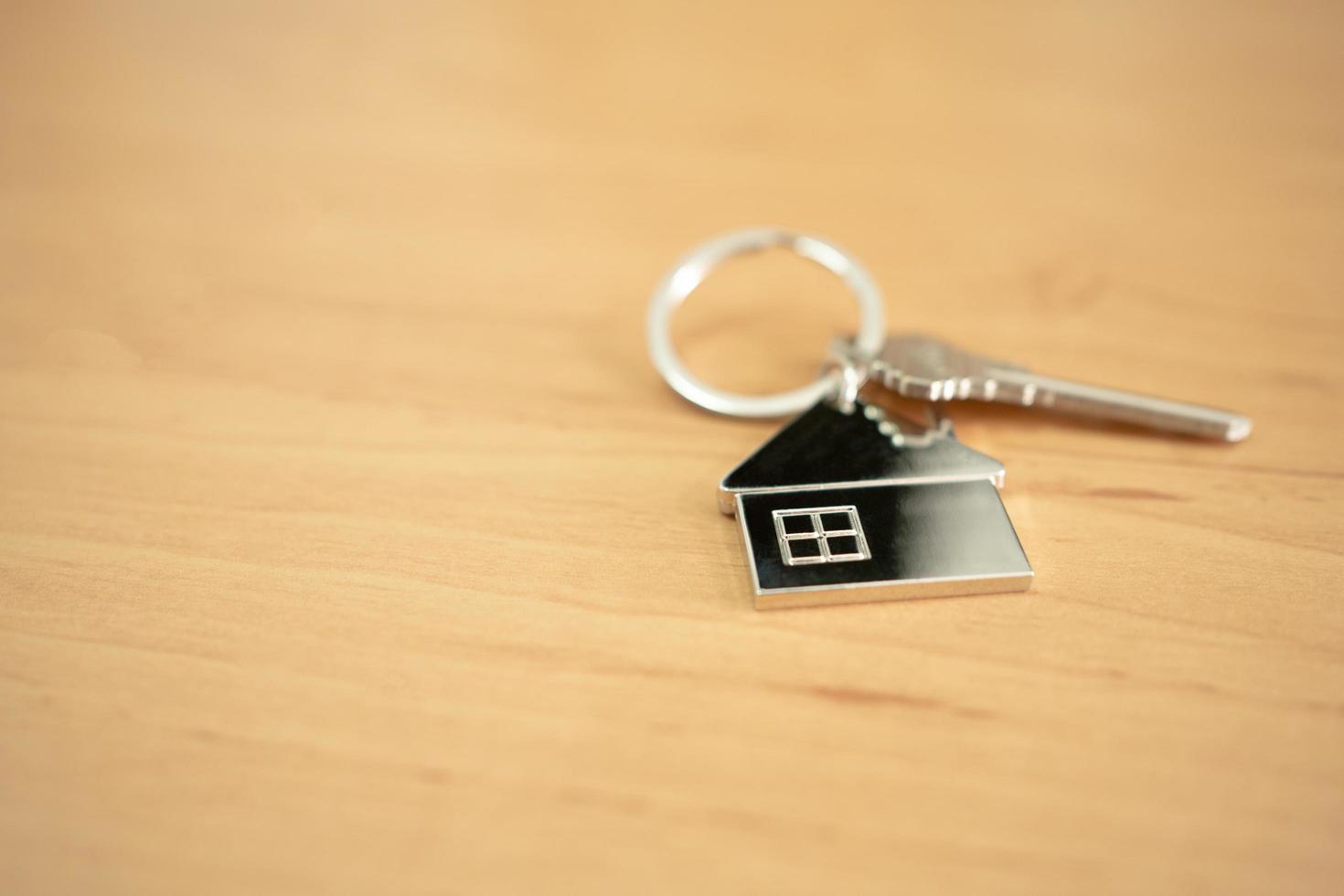 Selective focus at the home shape iron key chain with the key that put on wood table surface inside of the house. Home ownership, mortgage or property loan finance concept with copy space for text. photo