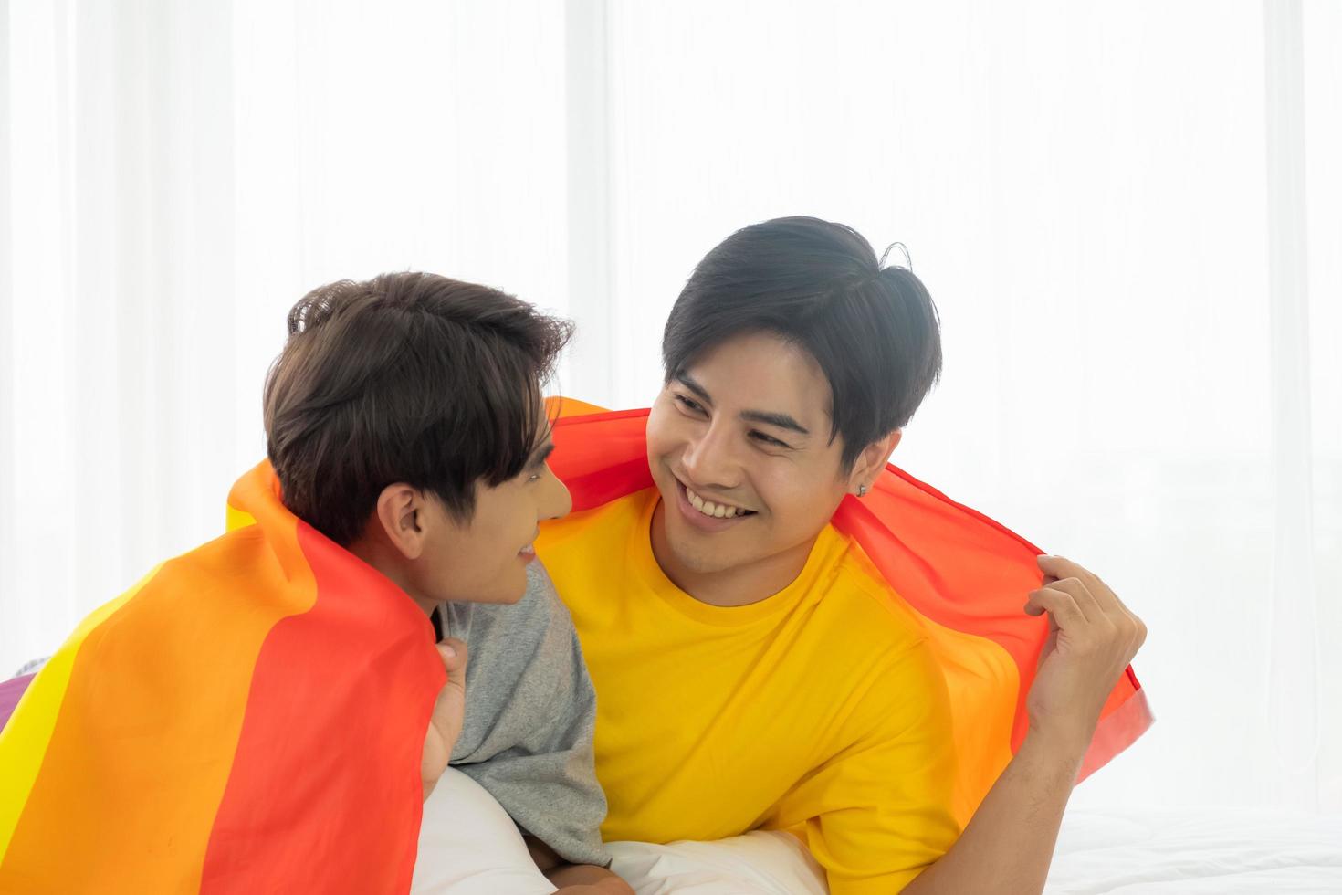 Selective focus at face. Handsome young Asian gay homosexual couple. Hug and embrace on the bed. With rainbow flag as LGBT sign. Gender equality and right. Romantic moment, same sex relationship. photo