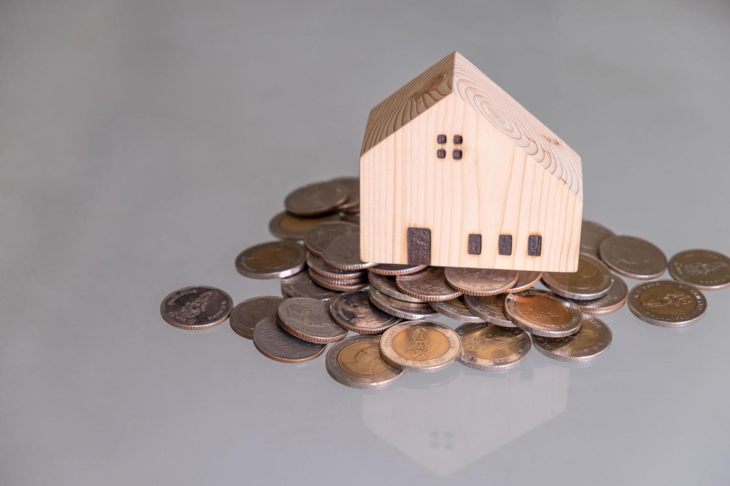 Selective focus at wooden house mock up that put on the top of growth money coins stack on the glass table with blurred background. Wealth and saving for home ownership and financial concept. photo