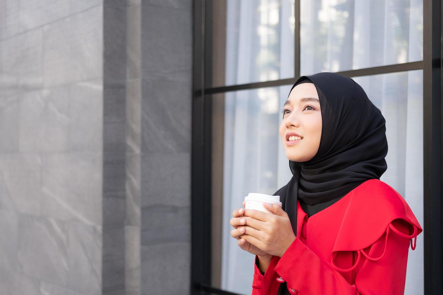 hermosas mujeres islámicas del este de Asia usando hiyab con vestido formal. sosteniendo una taza de café y caminando en el área urbana de la ciudad, sintiéndose feliz y sonriendo. concepto de estilo de vida de las personas con espacio de copia. foto