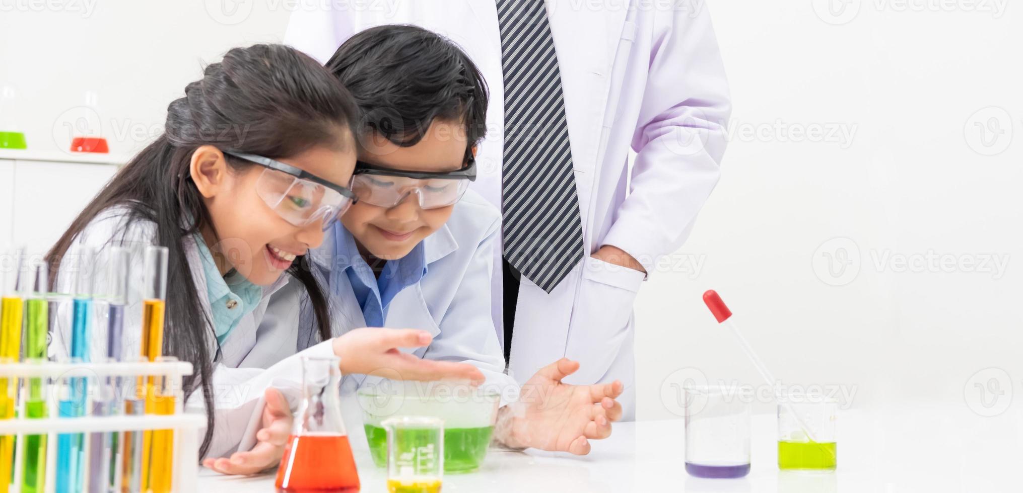 Young Asian boy and girl student wearing protective google while study and do science experiment in classroom with teacher. Learning and having fun moment. Chemist or biology classroom concept. photo