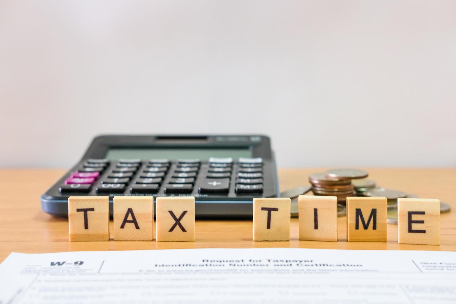 Selective focus at wood tax time sign with blurred calculator and coins stack and white copy space background. Business or personal tax payment, expense that need to manage and plan. photo