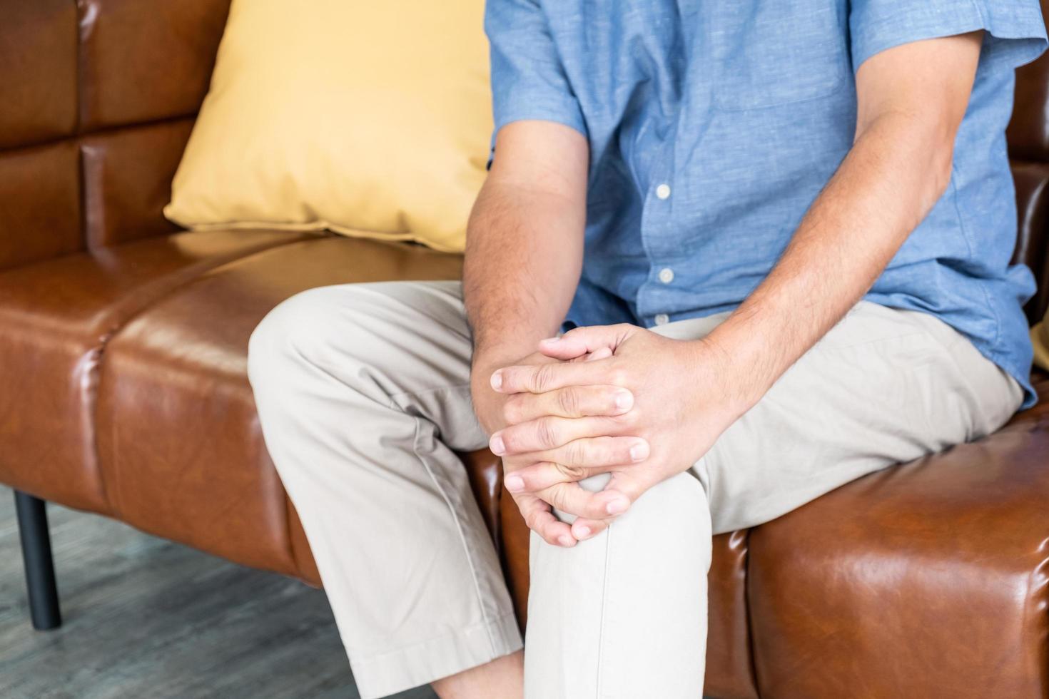 Selective focus at hand of old senior Asian man sitting at sofa touching knee and suffer from the pain and injury. Healthcare and medical problem of Elder people concept. photo