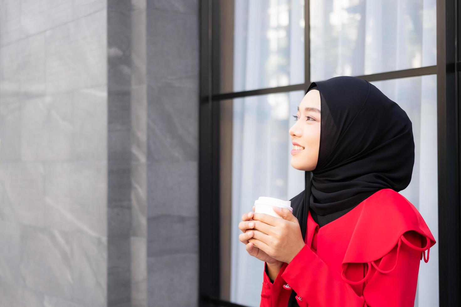 Beautiful East Asian Islamic women wearing hijab with formal dress.  Holding coffee cup and walking in urban city area, feeling happy and smile. People lifestyle concept with copy space. photo