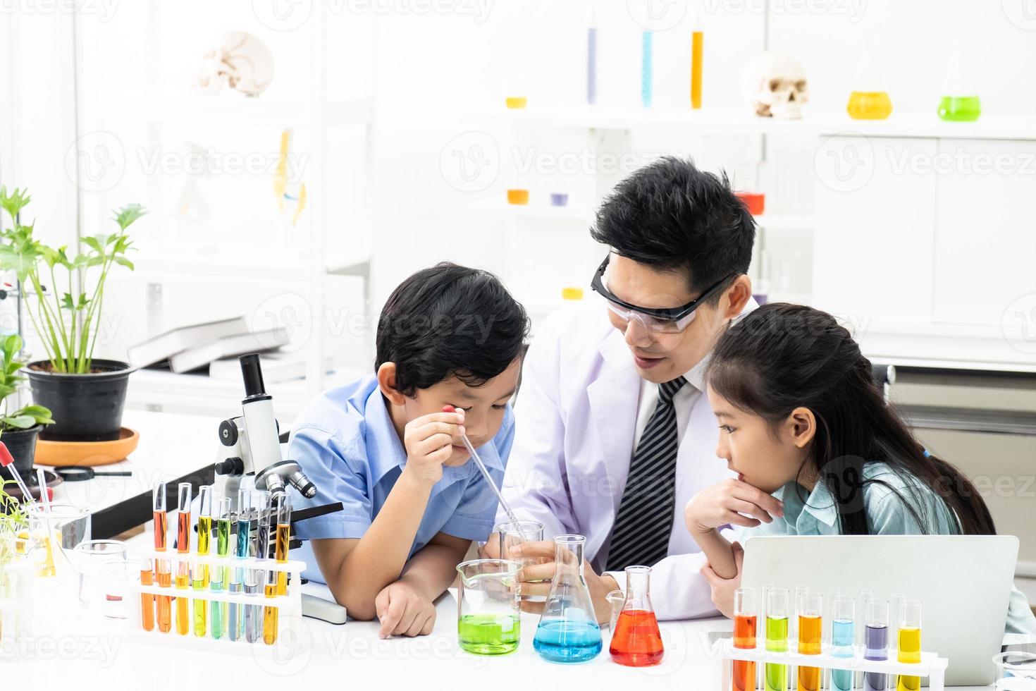 Selective focus at face. Young Asian boy and girl smile and having fun while doing science experiment in laboratory classroom with Teacher. Study with scientific equipment and tubes. Education concept photo