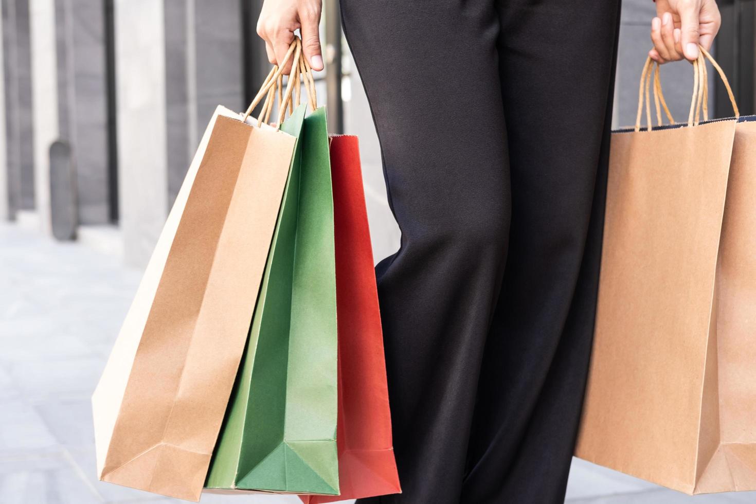 Selective focus at colorful shopping bags. Women carry many shopping back and walking out from fashion department store. End of year season sale that customer have high volume purchase. photo