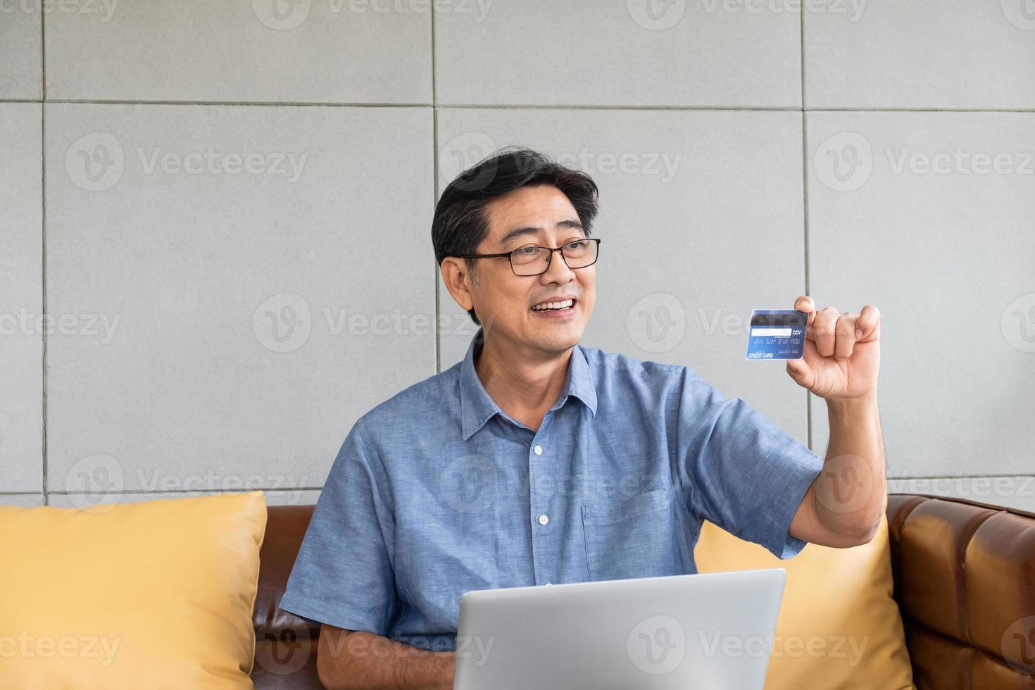 Selective focus at credit card. Senior Asian men hand holding credit card and fill in payment information for online shopping. Wireless internet technology with elderly concept. photo