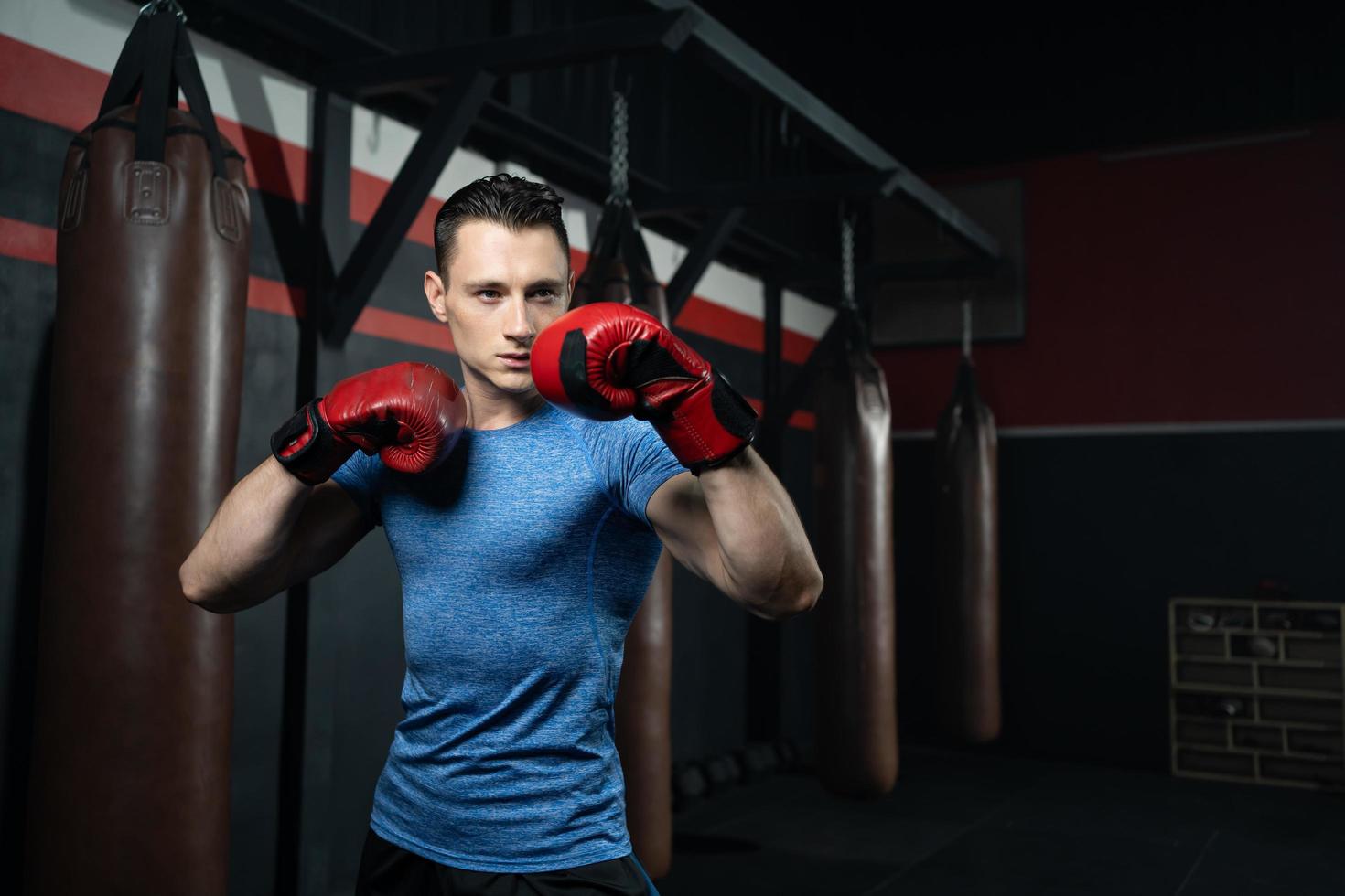 boxeador de hombres caucásicos guapos sin camisa con un fuerte golpe de boxeo de entrenamiento muscular en el costado del gimnasio con saco de arena. actividad de entrenamiento deportivo cardiovascular para una buena salud y desarrollar el cuerpo y la fuerza física. foto