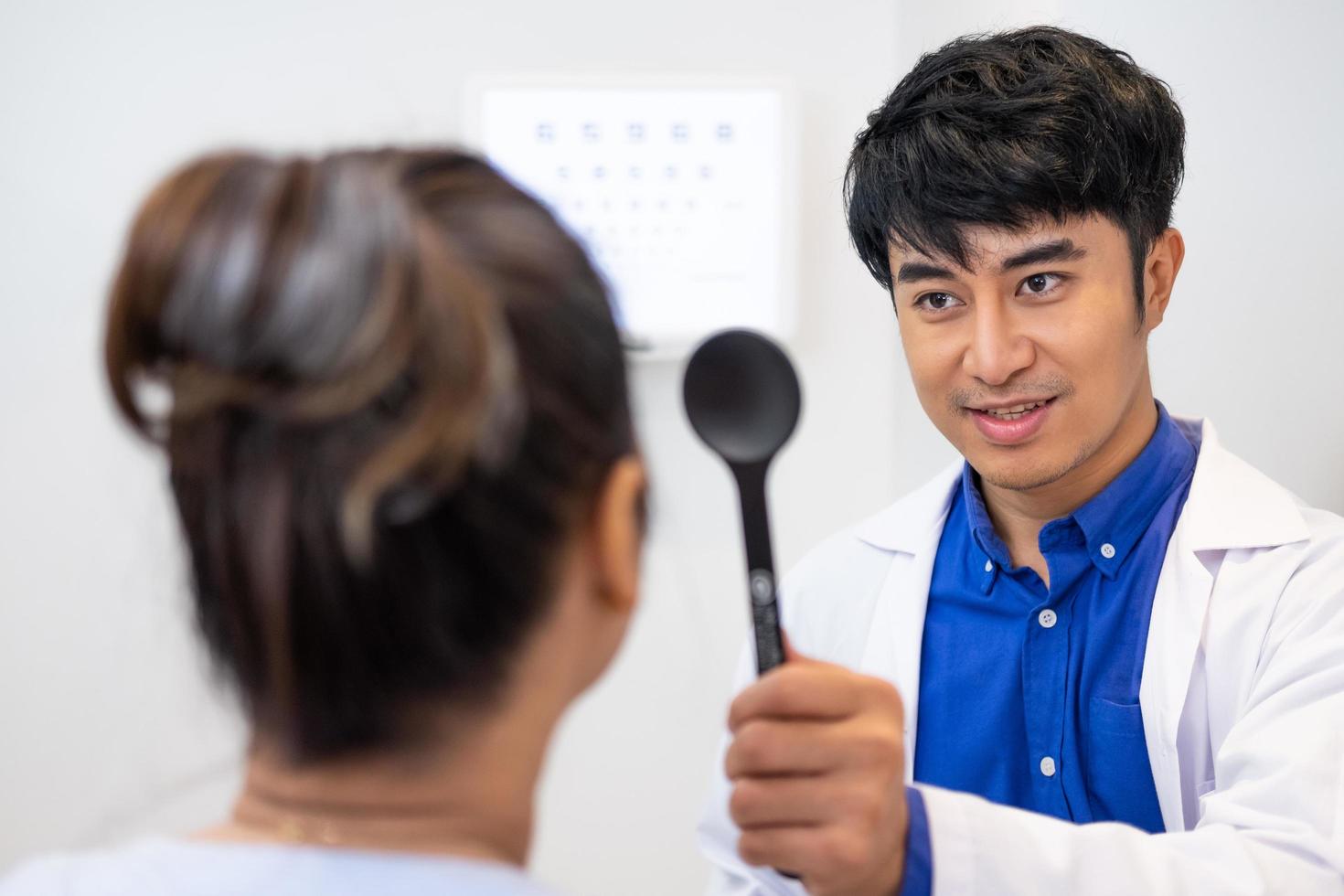 Selective focus at Optometrist face. While doctor using penlight and subjective refraction to  examine eye visual system of elder patient women with professional machine before made glasses. photo