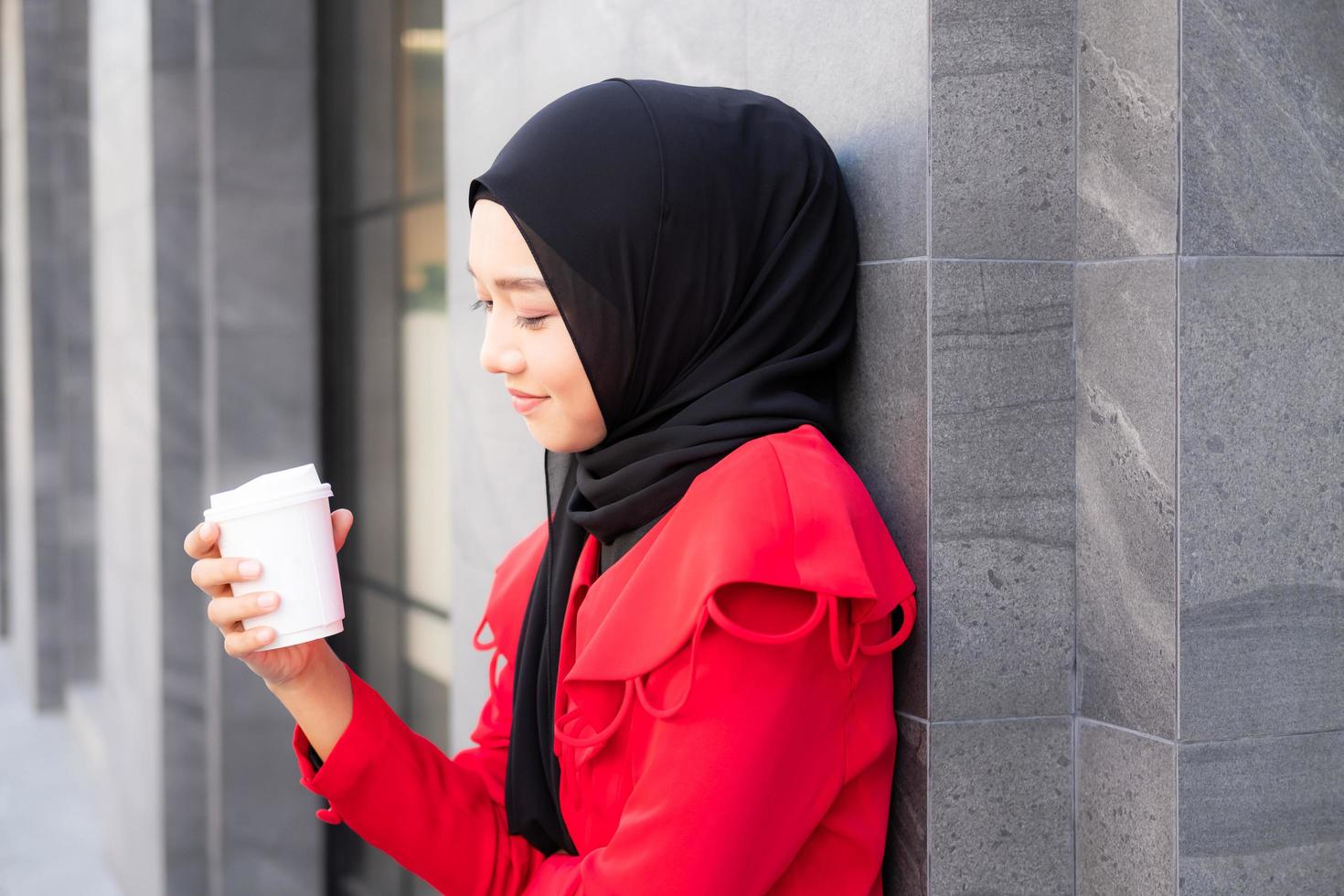 Beautiful East Asian Islamic women wearing hijab with formal dress.  Holding coffee cup and walking in urban city area, feeling happy and smile. People lifestyle concept with copy space. photo