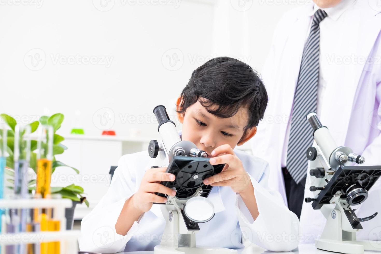 Young Asian element student adjust and using microscope in science class to examine  the lif subject with teacher.  Education and children learning or do experiment in classroom concept. photo