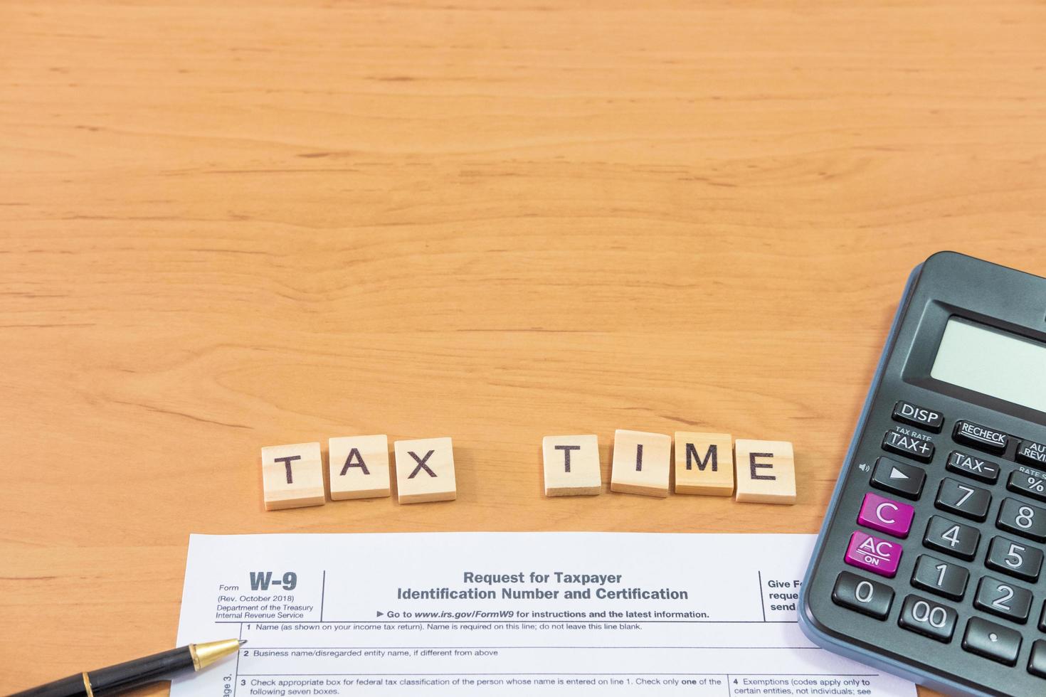 Selective focus at wood tax time sign with blurred calculator and coins stack and white copy space background. Business or personal tax payment, expense that need to manage and plan. photo