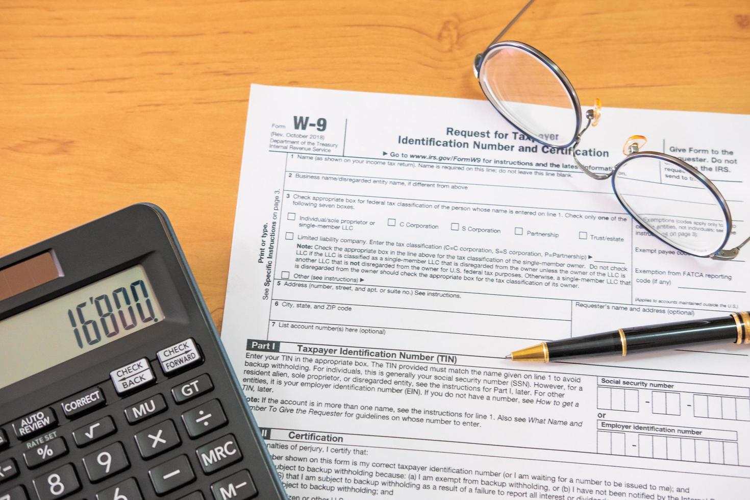 Selective focus Calculator button. American US tax form on wooden table. With blurred calculator, pen and glasses. Taxation time obligation for people who has income that need to comply to regulation. photo