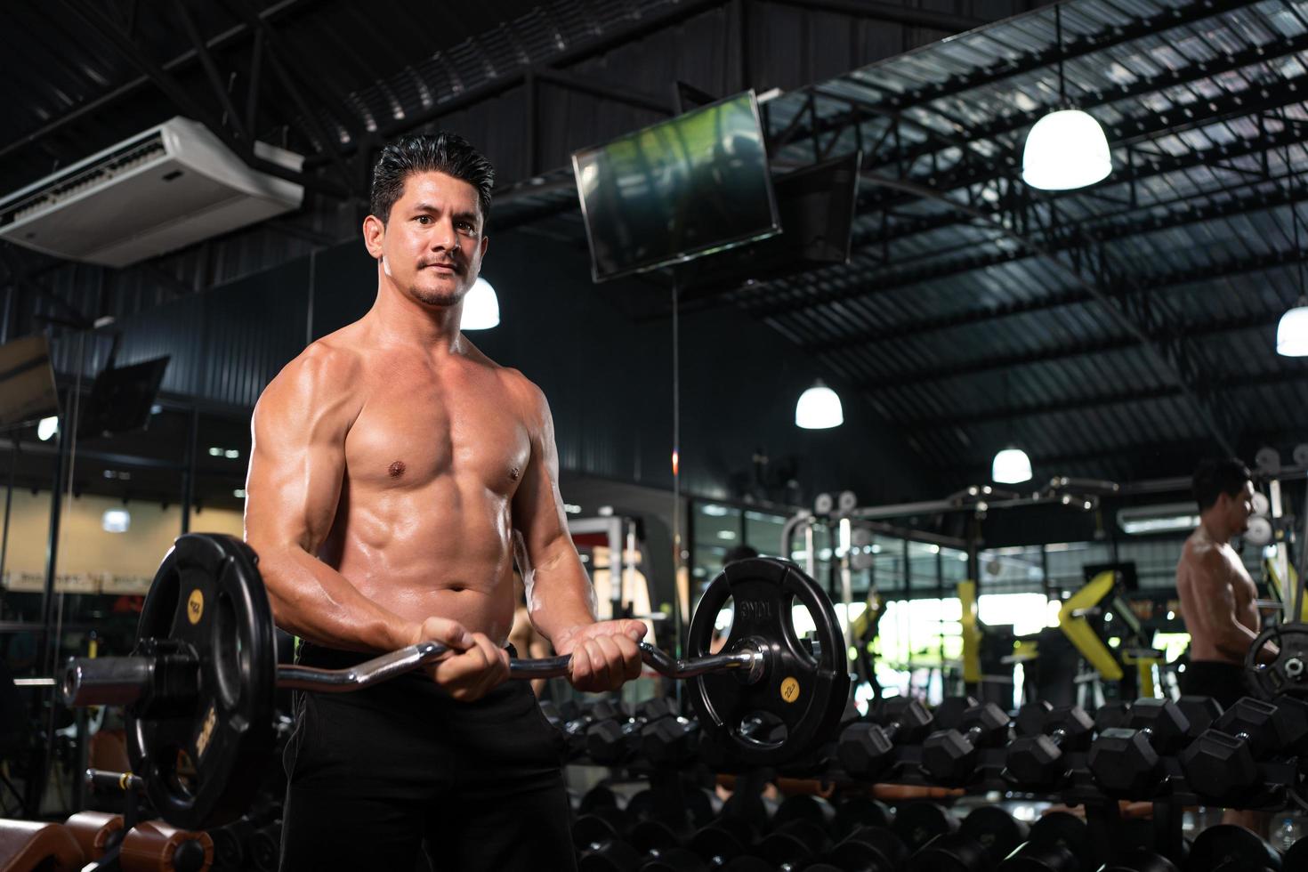 hombre adulto sin camisa levanta pesas para hacer ejercicio de culturismo y levantamiento de pesas dentro del gimnasio para entrenar la fuerza corporal y los músculos firmes de los brazos y la buena salud física del cuerpo. foto