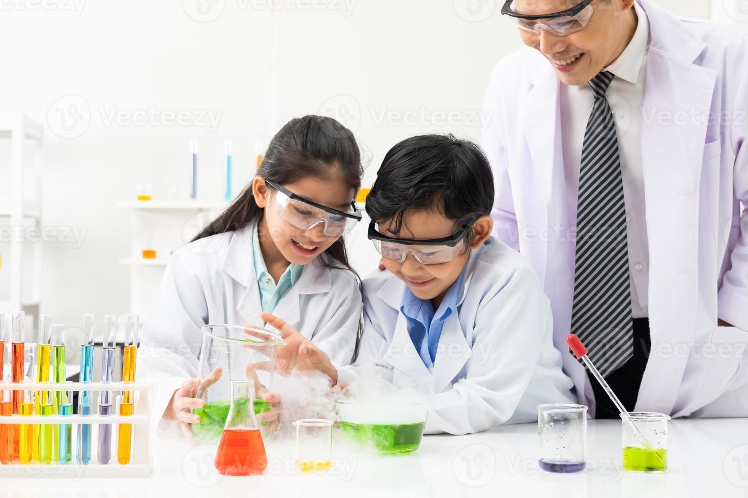 Young Asian boy and girl student wearing protective google while study and do science experiment in classroom with teacher. Learning and having fun moment. Chemist or biology classroom concept. photo