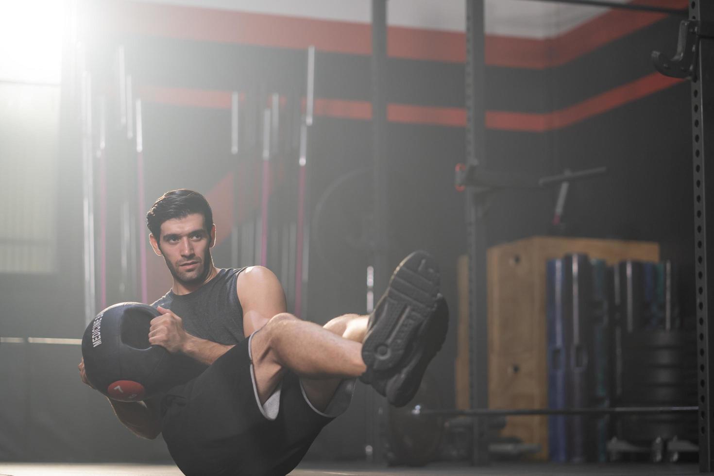 Handsome adult Caucasian men using weight ball to do crossfit exercise inside of fitness gym to workout for firm abs or stomach muscle and good body health. photo