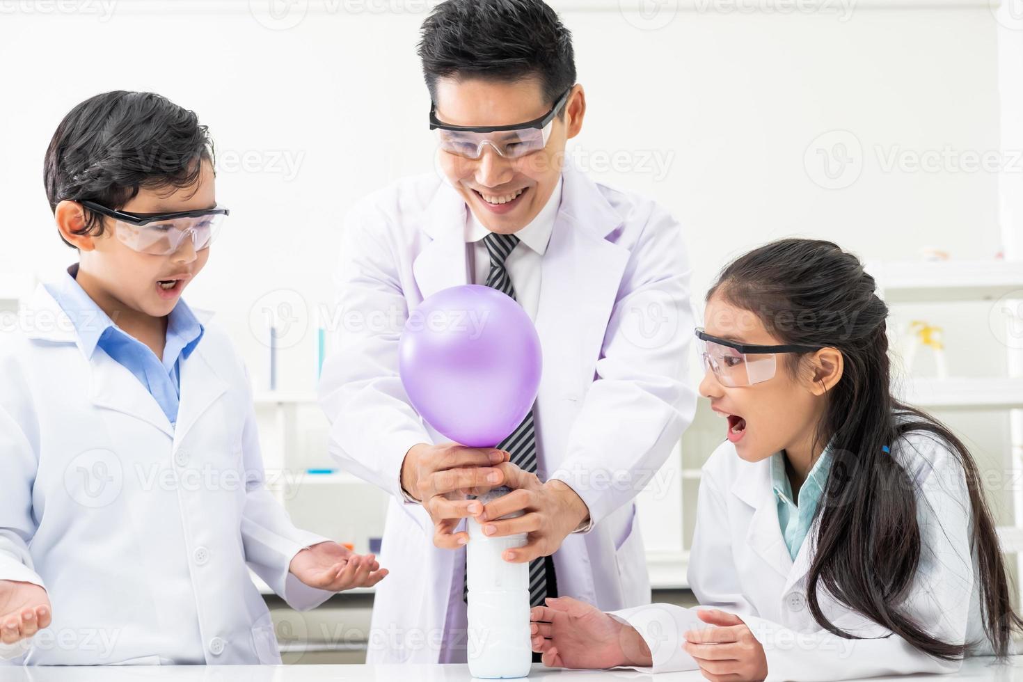 enfoque selectivo en la cara de la niña. un niño y una niña asiáticos sonríen y se divierten mientras hacen experimentos científicos en el aula de laboratorio con el maestro. estudio con equipo científico y tubos. foto