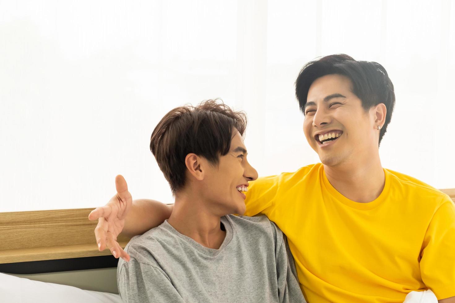 Selective focus at face. Good looking Asian gay homosexual couple hug and smile while using Digital tablet smartphone, showing love expression on the bed. LGBT relationship concept with copy space. photo