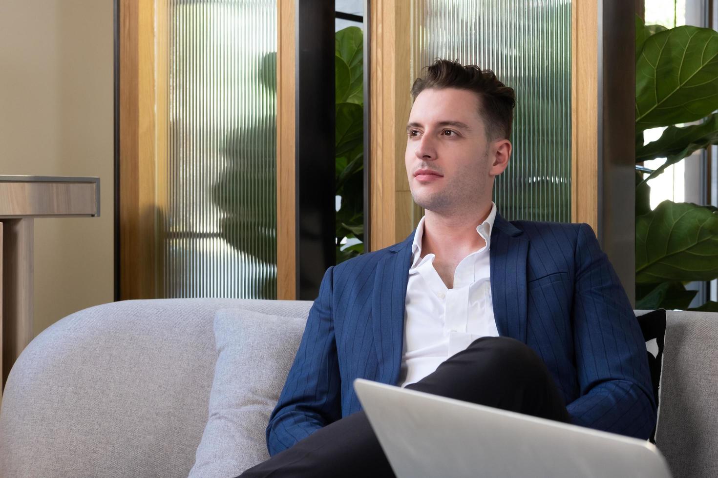 Adult Caucasian businessman dress in smart formal suit sitting inside modern office space drinking coffee while waiting and planning for business meeting. Entrepreneur concept with copy space. photo