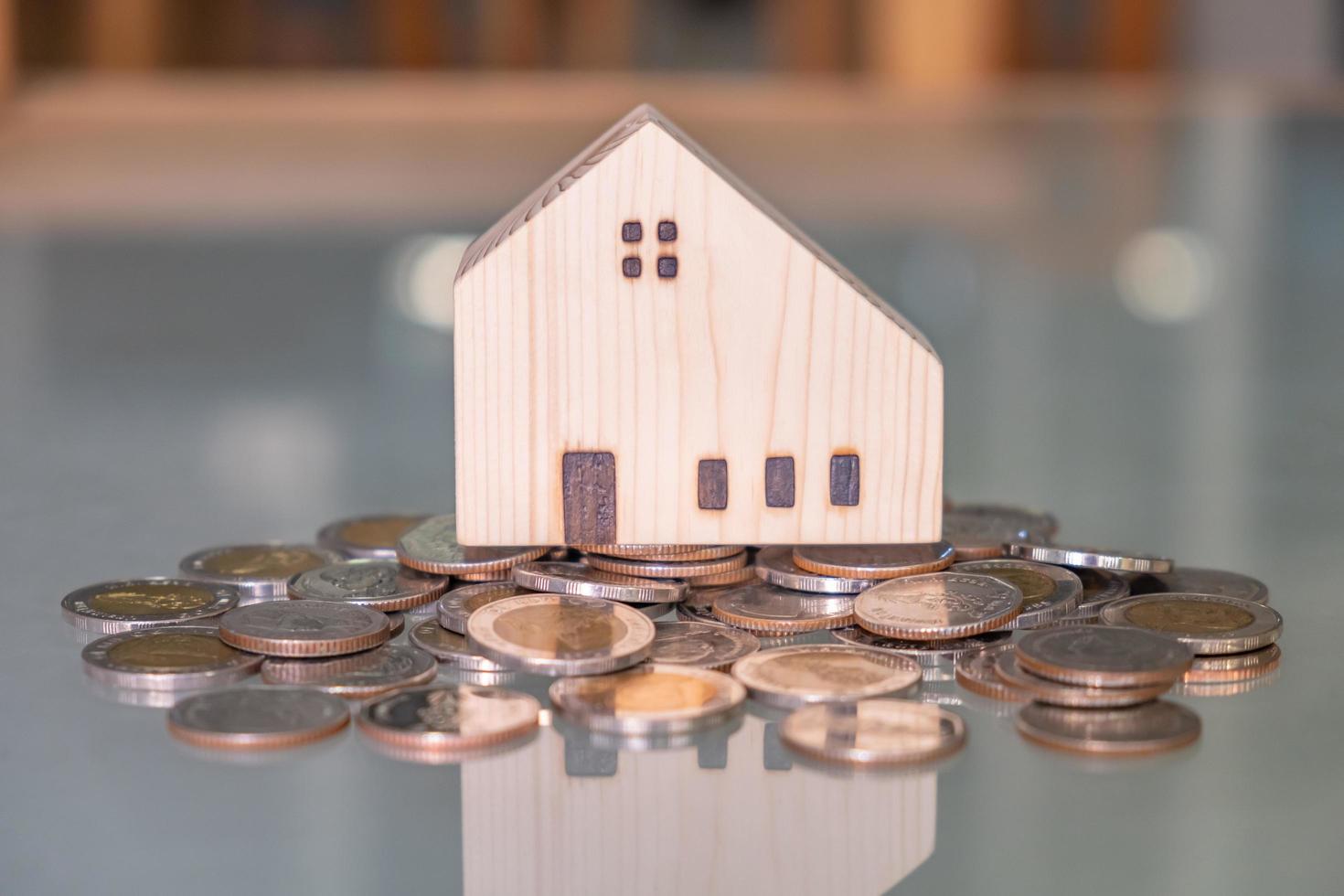 Selective focus at wooden house mock up that put on the top of growth money coins stack on the glass table with blurred background. Wealth and saving for home ownership and financial concept. photo