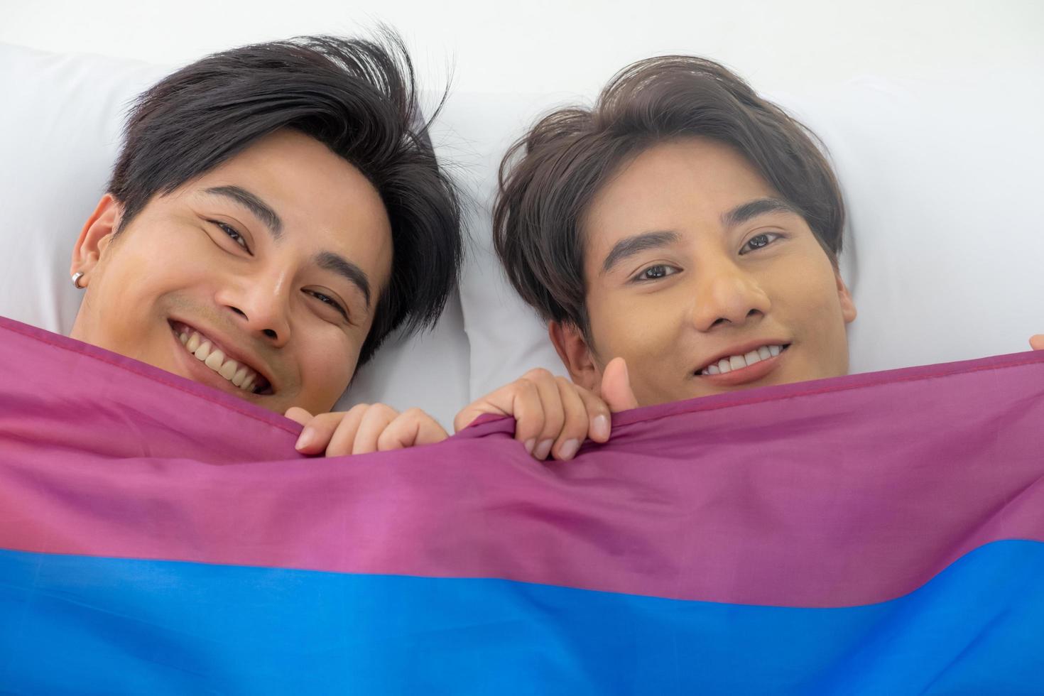 Selective focus at face. Handsome young Asian gay homosexual couple. Hug and embrace on the bed. With rainbow flag as LGBT sign. Gender equality and right. Romantic moment, same sex relationship. photo