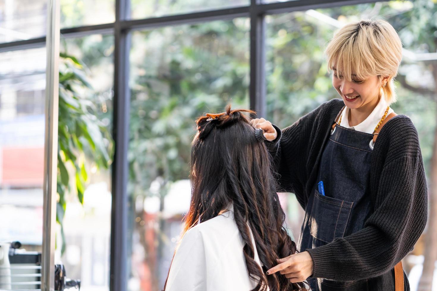 Selective focus at face of women Hair stylish smiling while do hairdressing and put care treatment while styling curly hair for client. Professional occupation, beauty and fashion service. photo