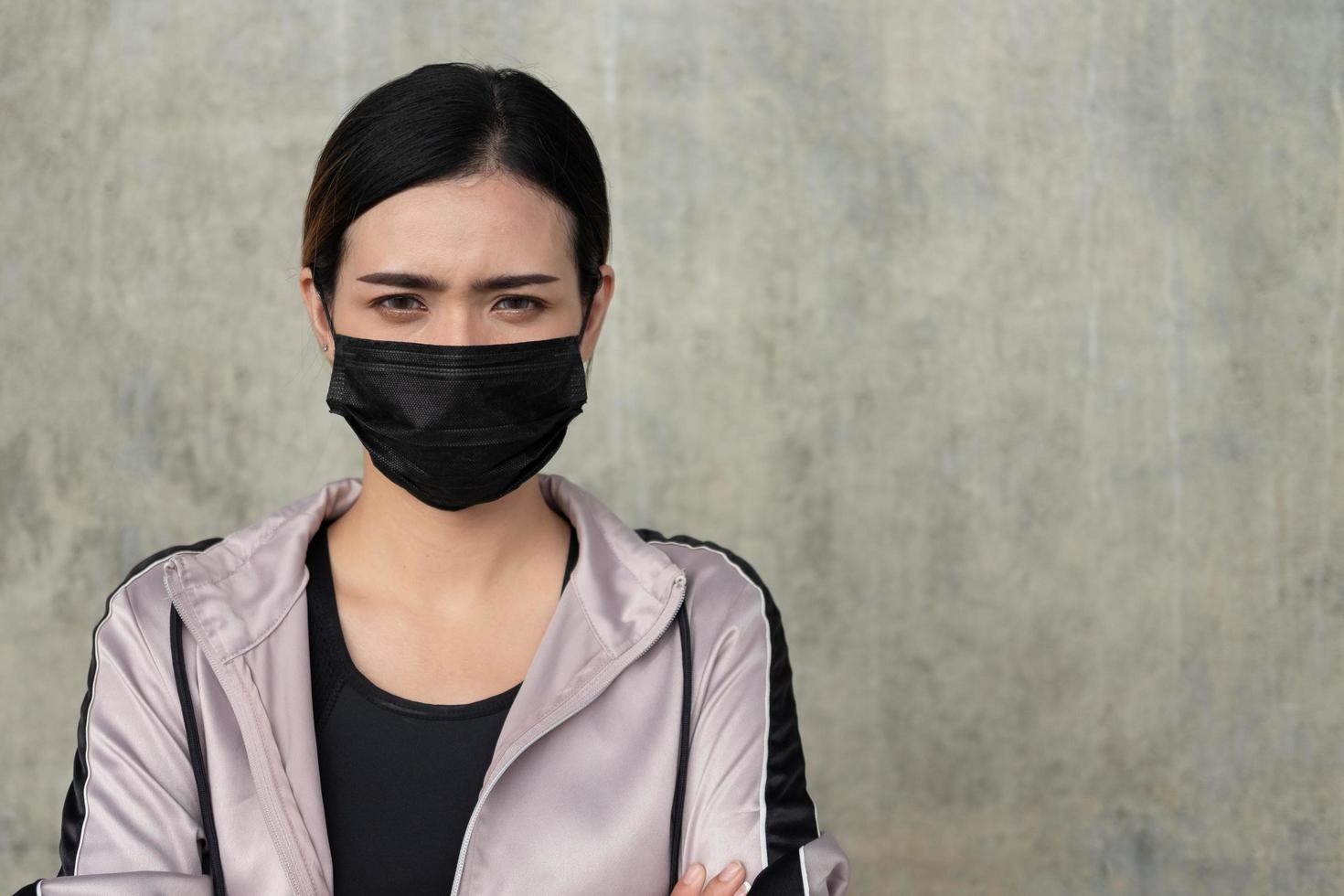 Selective focus at face of young beautiful Asian women wearing surgical face mask with serious or stress emotion before exercise or running at the city park in the morning. New normal lifestyle. photo