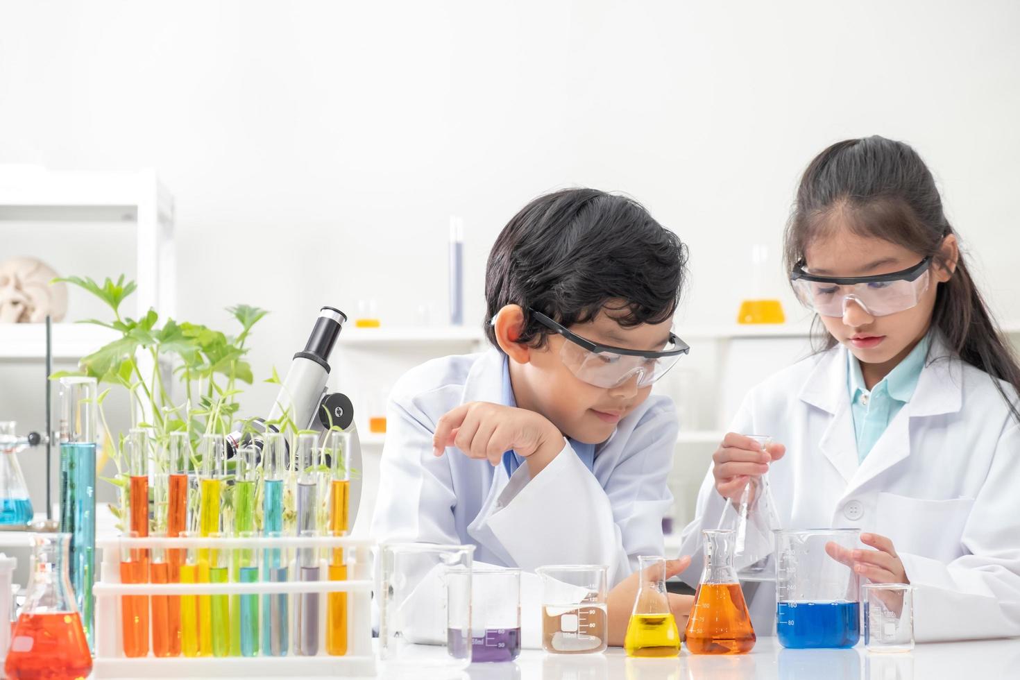 un niño y una niña asiáticos sonríen y se divierten mientras hacen experimentos científicos en el aula de laboratorio con el maestro. estudio con equipo científico y tubos. concepto de educación foto