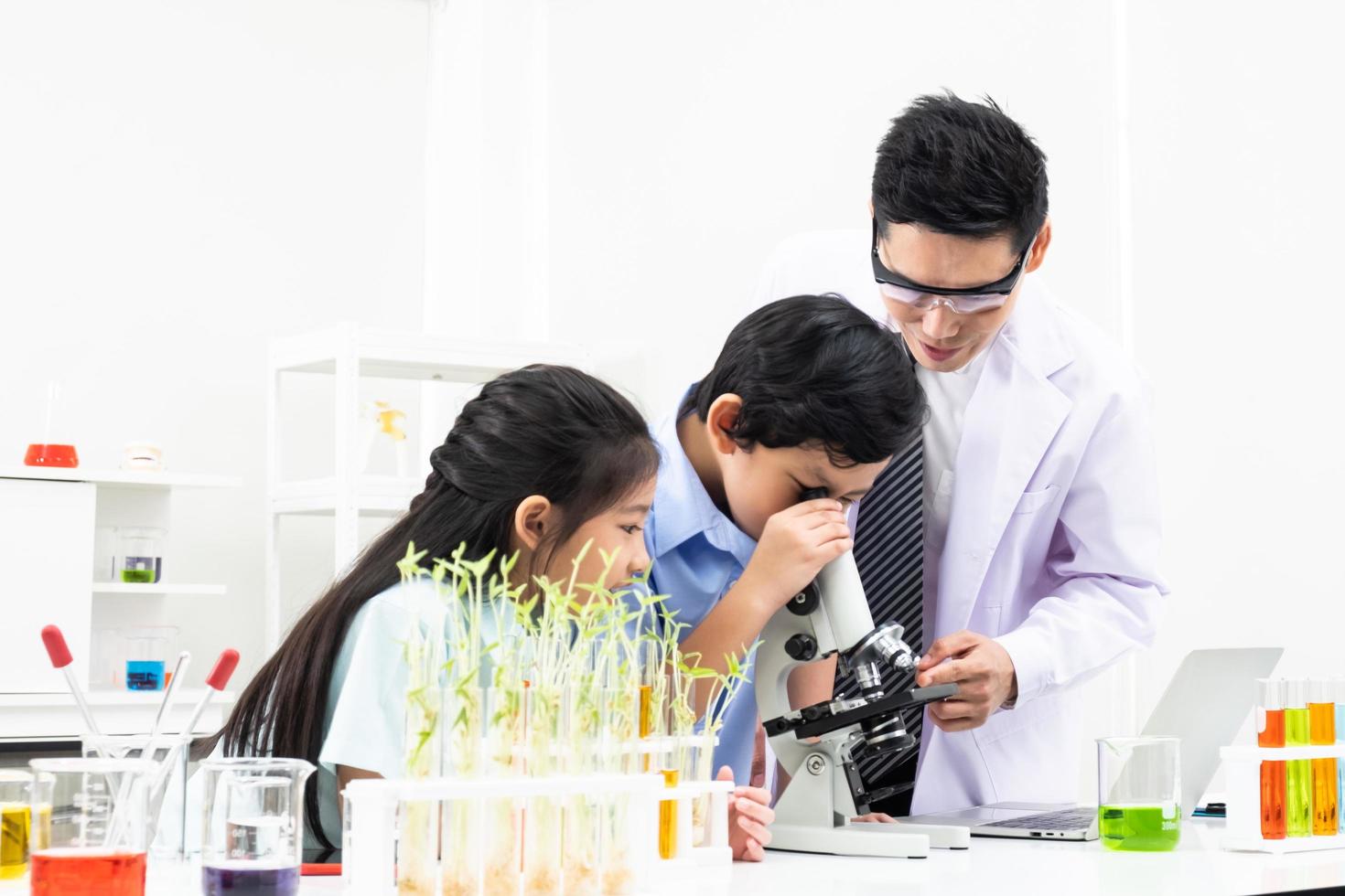 Selective focus at face. Young Asian boy and girl smile and having fun while doing science experiment in laboratory classroom with Teacher. Study with scientific equipment and tubes. Education concept photo