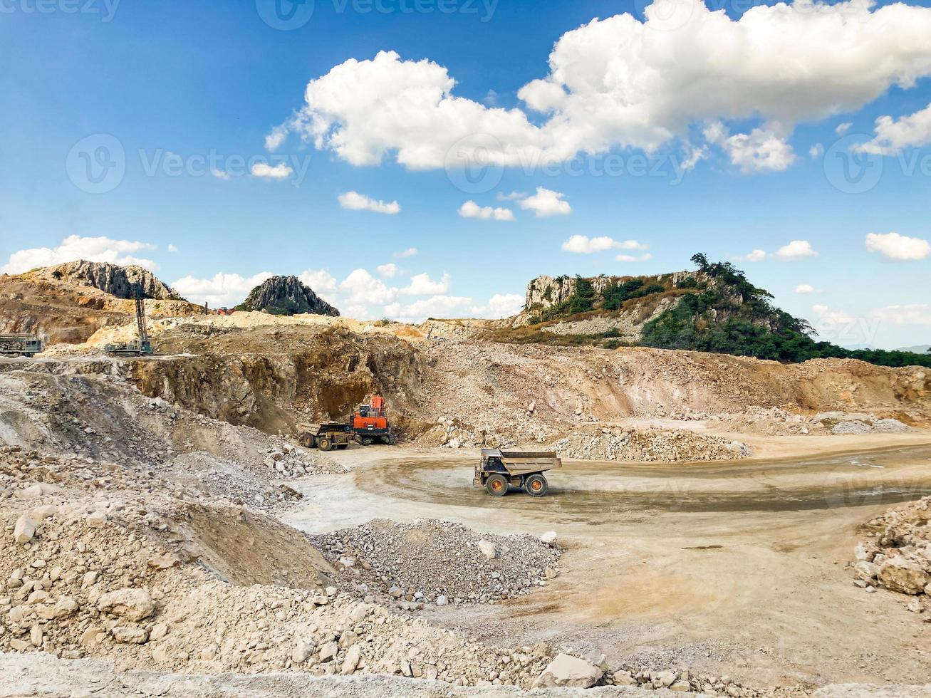 toma de paisaje de roca y mina de hormigón que rodea con piedra, montaña y cielo azul. con un ingeniero industrial que supervisa a un trabajador que conduce un camión y una máquina perforadora. concepto industrial. foto