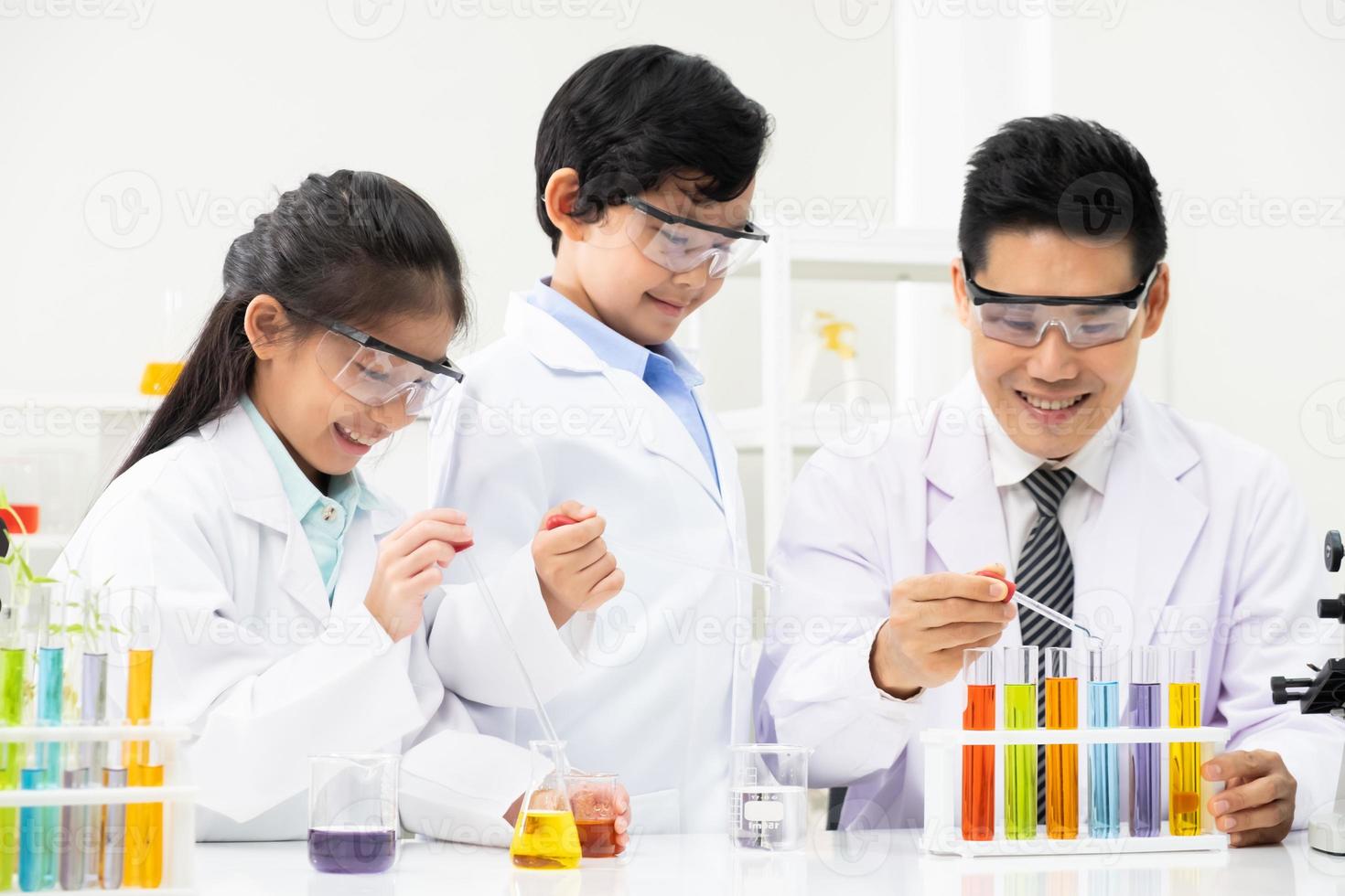 Selective focus at face. Young Asian boy and girl smile and having fun while doing science experiment in laboratory classroom with Teacher. Study with scientific equipment and tubes. Education concept photo