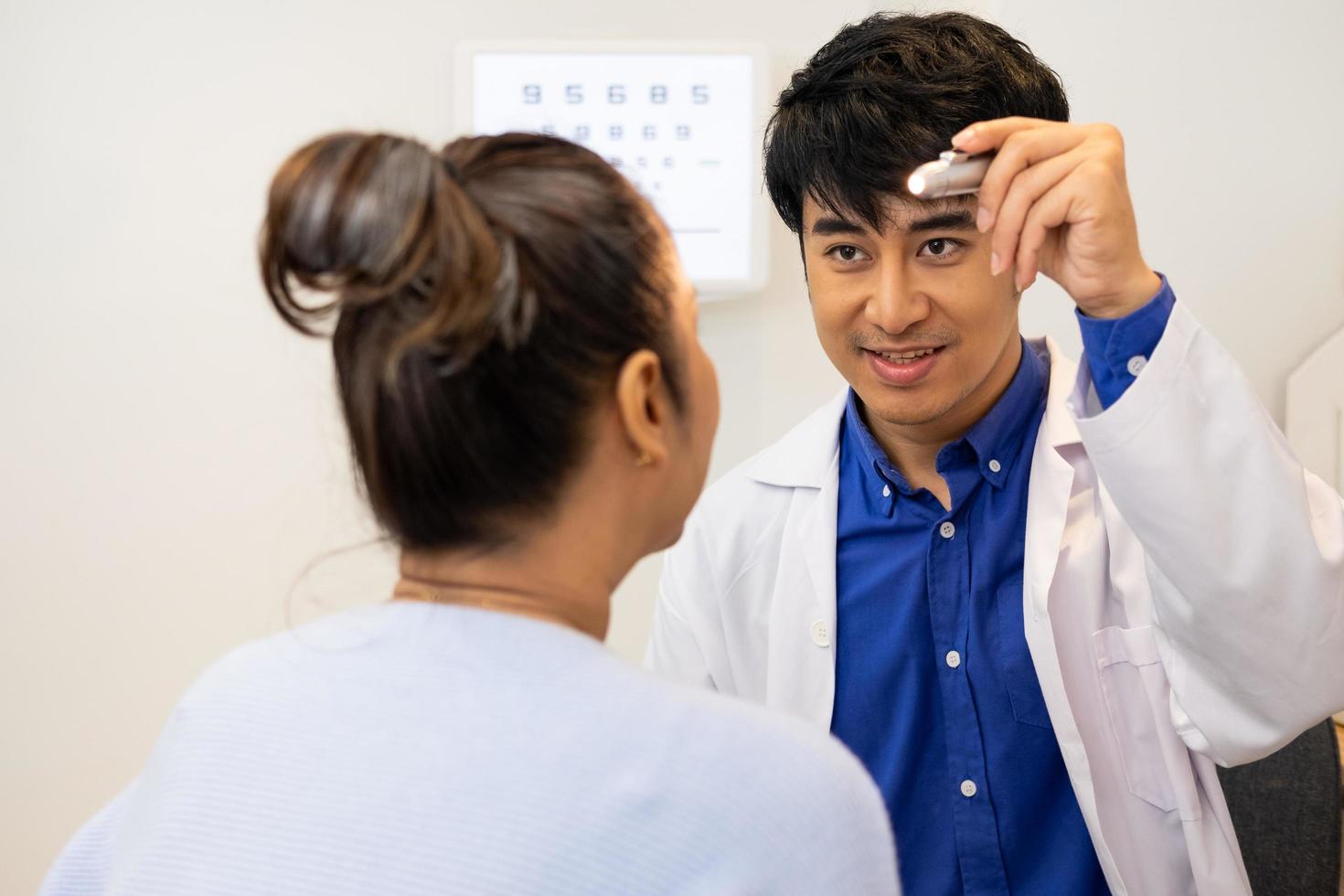 Selective focus at Optometrist face. While doctor using penlight and subjective refraction to  examine eye visual system of elder patient women with professional machine before made glasses. photo