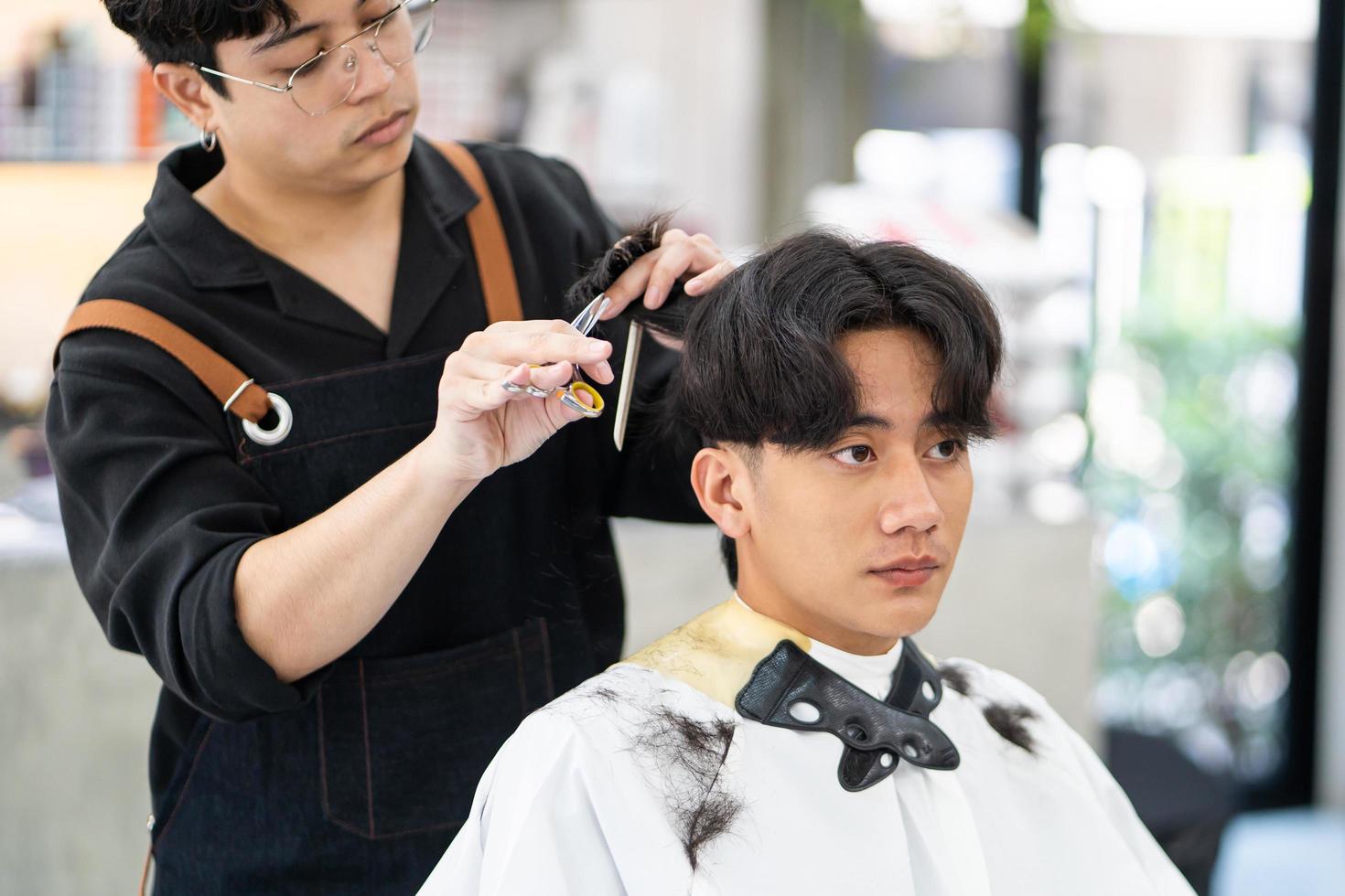Selective focus at customer. Asian men Hair stylish with customer while do hair cut while styling hair for client. Professional occupation, beauty and fashion service new normal photo