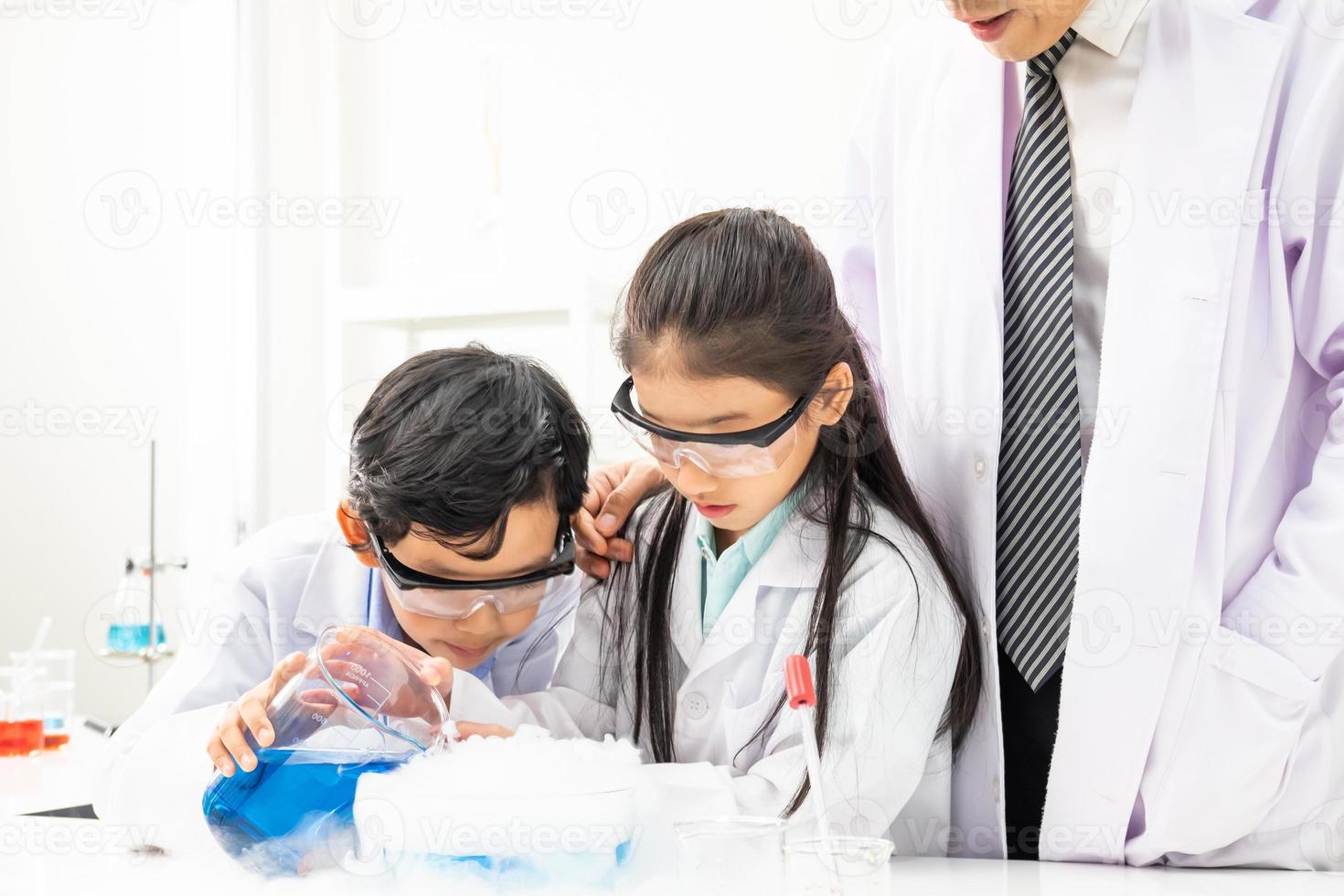 enfoque selectivo en la cara de la niña. un niño y una niña asiáticos sonríen y se divierten mientras hacen experimentos científicos en el aula de laboratorio con el maestro. estudio con equipo científico y tubos. foto