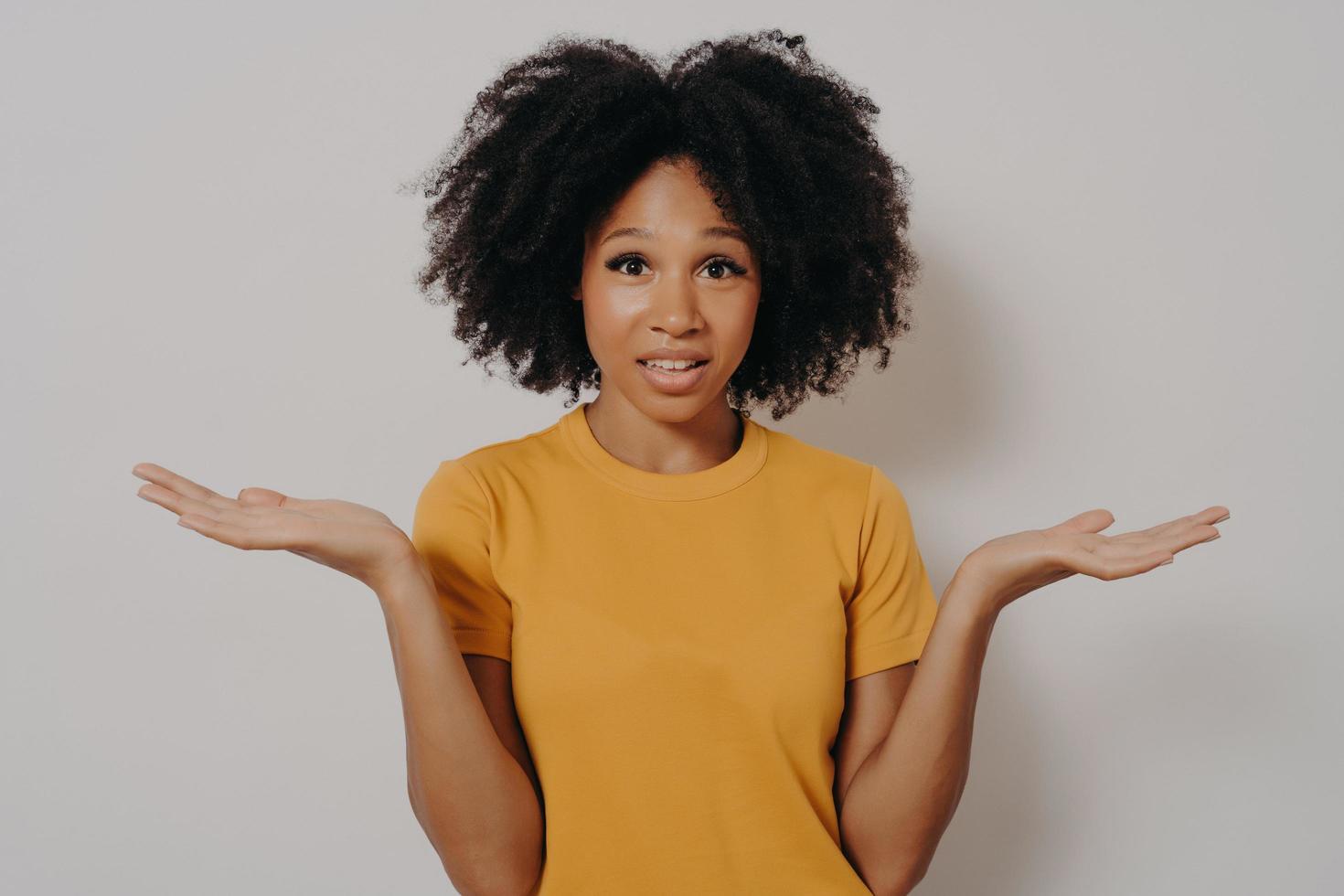 Confused doubtful black woman shrugging with shoulders, feeling baffled while looking at camera photo