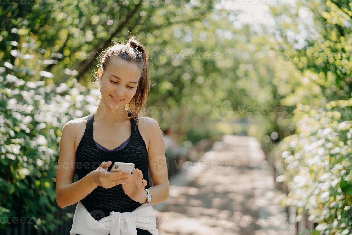 mujer adulta atlética activa en ropa deportiva realiza un seguimiento de la actividad física a través de un teléfono inteligente monitorea la salud con la mejor aplicación de fitness tiene poses de cabello peinado oscuro al aire libre. concepto de estilo de vida saludable deportivo foto