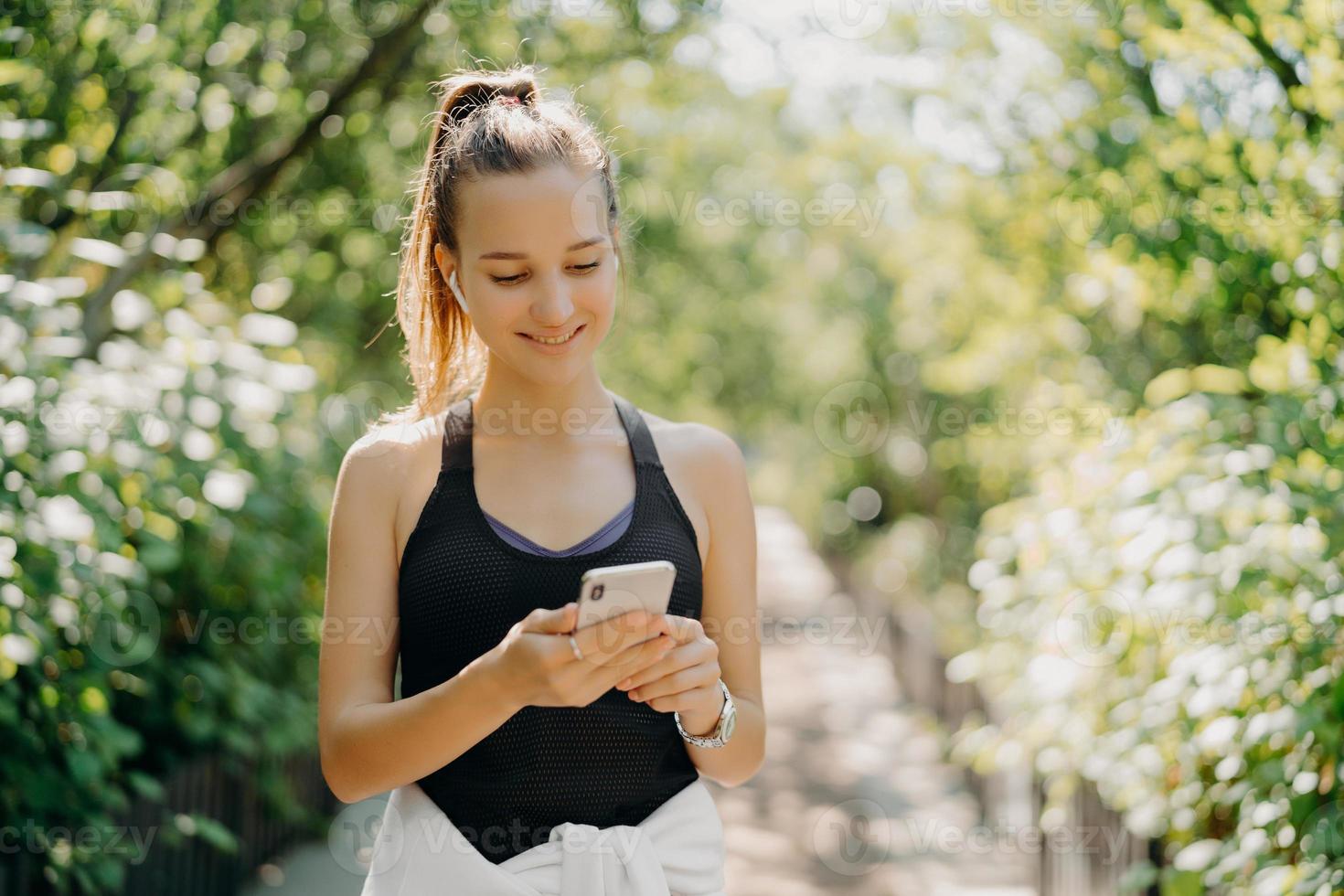 estilo de vida deportivo y concepto de entrenamiento. una joven deportista complacida usa un smartphone para chatear en línea y escuchar música descansa después de que el entrenamiento de cardio haya peinado la cola de caballo vestida con ropa activa foto