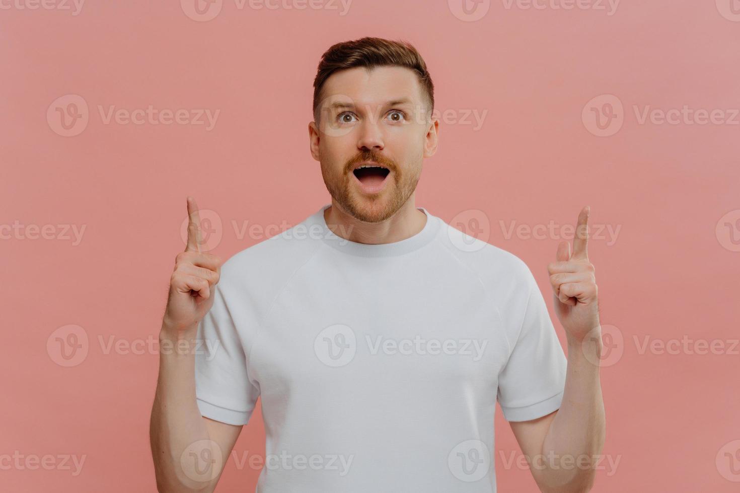 Excited young man pointing with two forefingers up and with shocked face expression photo