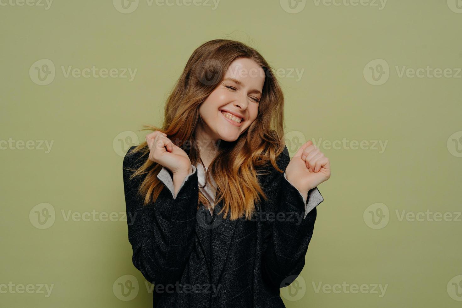 Happy young woman with closed eyes holding hands up with excitement photo