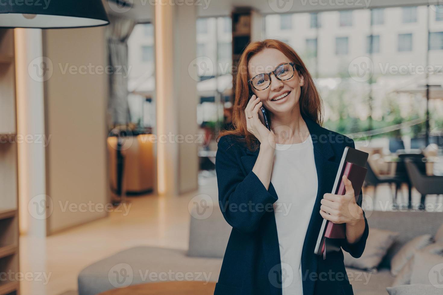 sonriente hermosa pelirroja gerente de negocios haciendo llamadas de negocios en el trabajo foto