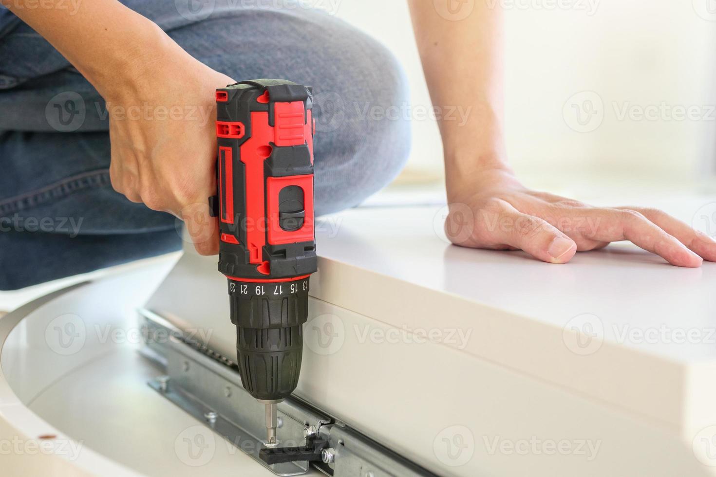 man assembling white table furniture at home using cordless screwdriver photo