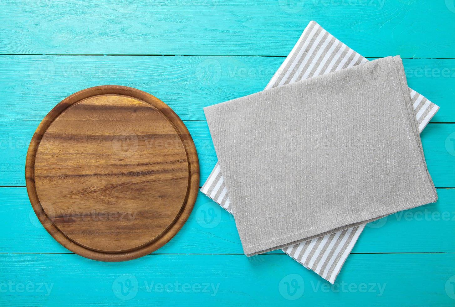 Frame of round cutting board on a striped and gray tablecloth on blue wooden background. Top view and place for text photo
