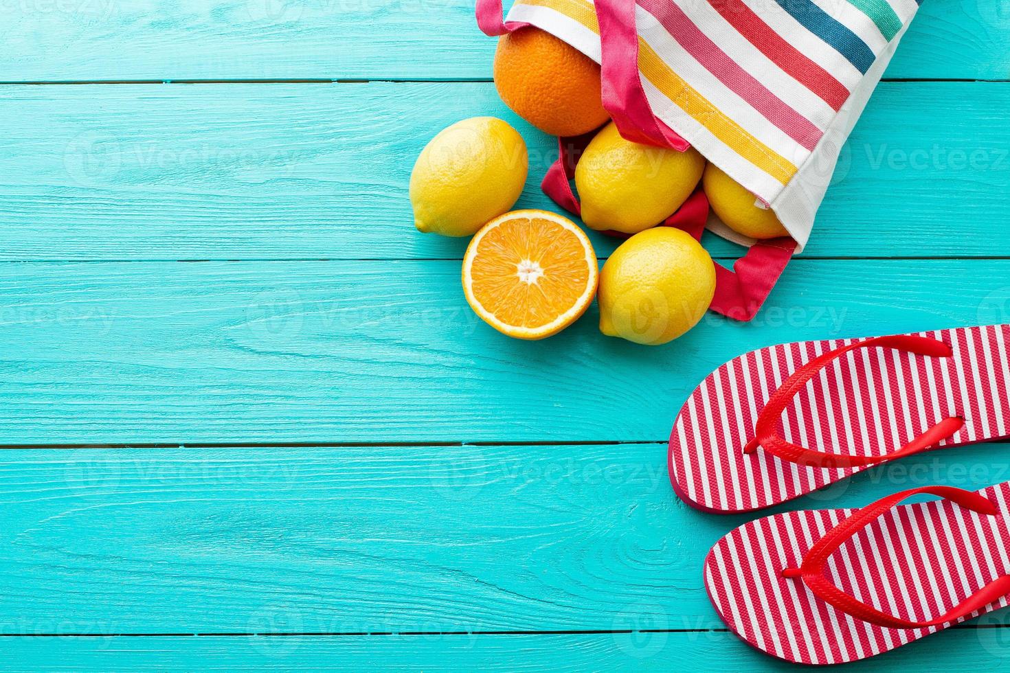 Summer fun time and fruits on blue wooden background. Mock up and picturesque. Orange, lemon fruit in bag and flip flops on the floor. Top view and copy space photo