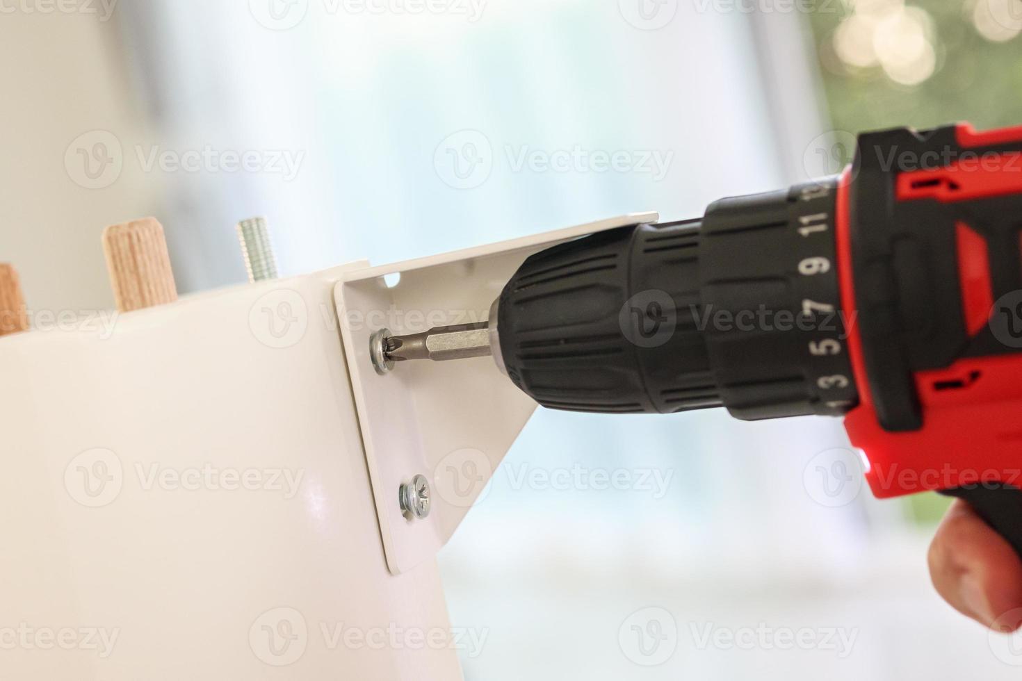 man assembling white table furniture at home using cordless screwdriver photo