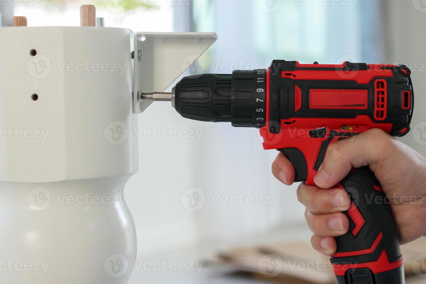 man assembling white table furniture at home using cordless screwdriver photo