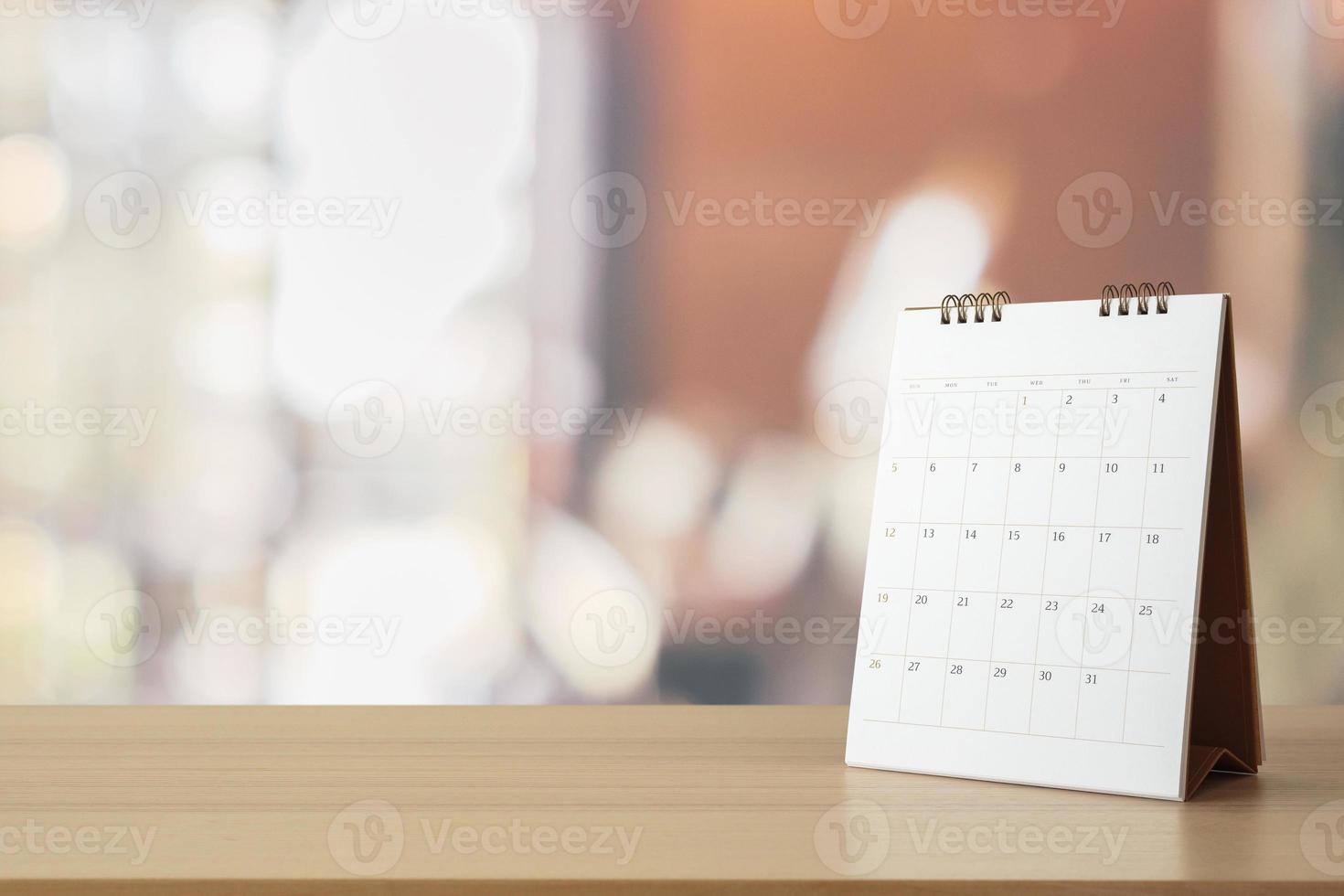 calendario de escritorio de papel blanco sobre una mesa de madera con una cita de fondo borrosa y concepto de reunión de negocios foto