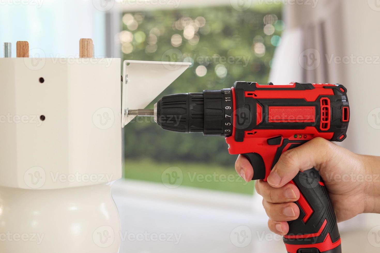 man assembling white table furniture at home using cordless screwdriver photo