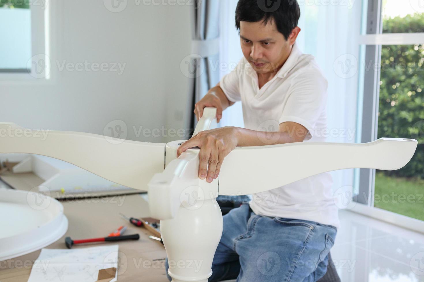 Asian man assembling white table furniture at home photo